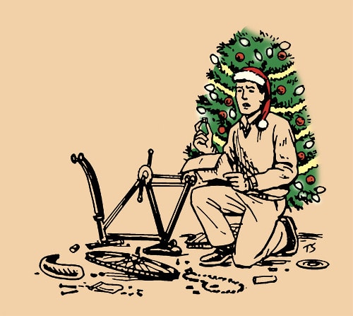 Man in santa hat assembling bicycle beside Christmas tree.