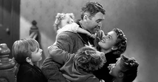 A black and white image of a man embracing a woman and three children, with greater joy and affection.