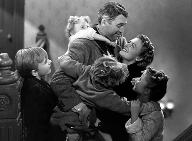 A black and white image of a man embracing a woman and three children, with greater joy and affection.