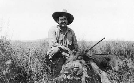 A man on an African Safari adventure, kneeling in the grass next to a majestic lion.