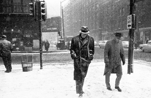 Vintage men walking in snowstorm in city wearing fedoras. 