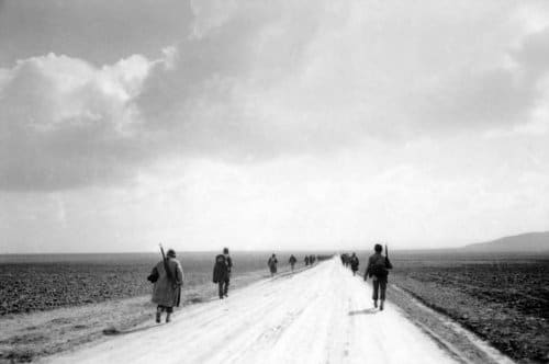 Vintage soldiers marching along dirt road desolate landscape .