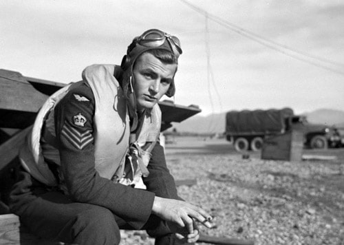 Vintage wwii pilot sitting in uniform smoking cigarette wearing aviator cap.