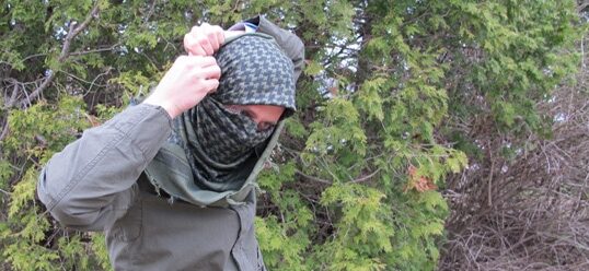 A man wearing a military-style balaclava in the woods.