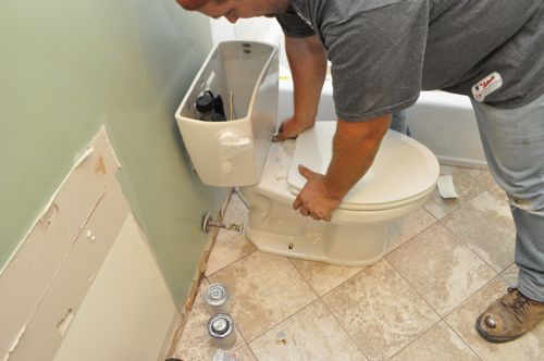Man installed a new toilet seat firmly pressing toilet onto floor. 