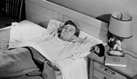 A twentysomething man laying in bed with a blanket on his head, showcasing his unique powers.