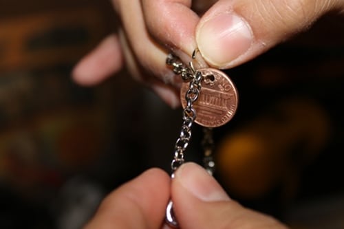Man attaching penny to chain bracelet for diy charm jewelry. 