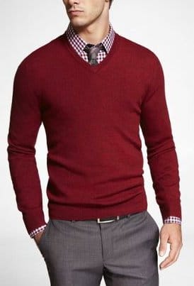 Man wearing red sweater layer over checked pattern long sleeve shirt and tie.