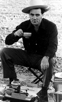Louis L'Amour sitting in chair drinking coffee cowboy hat.