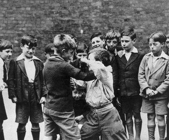A black and white photo depicting a group of boys engaged in a spirited fight.