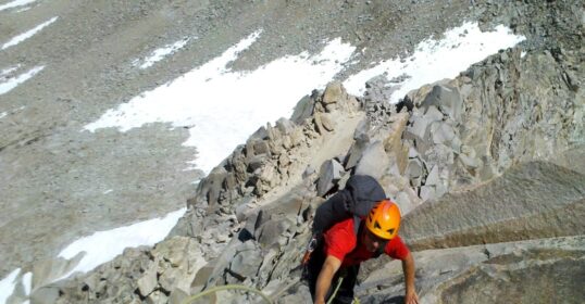 A Mountain Guide is leading a climber up a steep rocky slope.