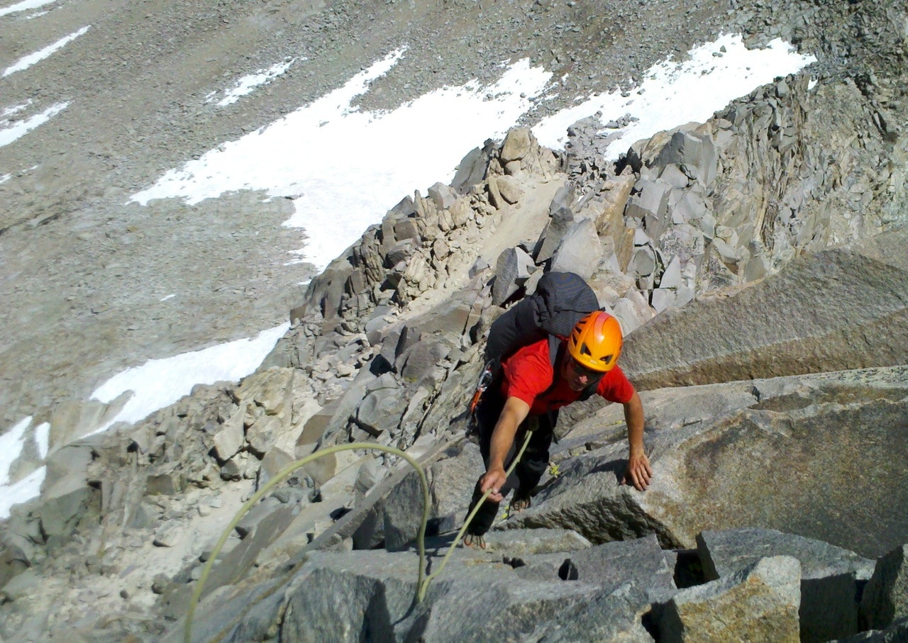 A Mountain Guide is leading a climber up a steep rocky slope.