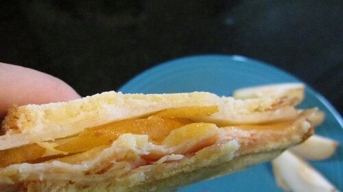 A person holding a turkey sandwich with Asian pears and pecans.