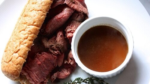 A homemade roast beef sandwich with au jus on a white plate.