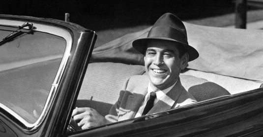 A gentleman in a hat behind the wheel of a convertible car, practicing proper driving etiquette.