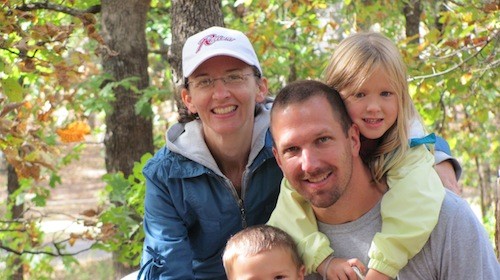 A man and woman pose with two children for a photo in the woods.