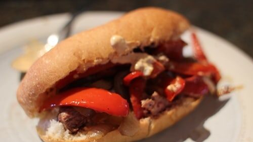 A Drunken Steak Sandwich with peppers and cheese on a plate.