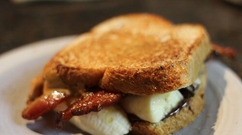 A grilled sandwich with bacon and banana, smeared with creamy peanut butter, on a plate.