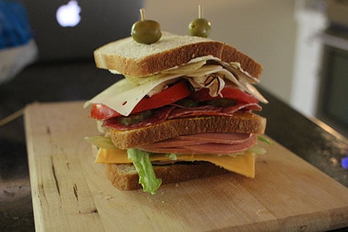 An All-American Dagwood sandwich is sitting on top of a cutting board.