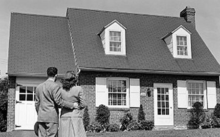 A black and white photo of a couple standing in front of their first home.
