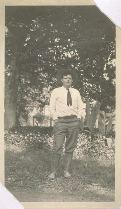 Jack London standing outdoors with hat and short tie.