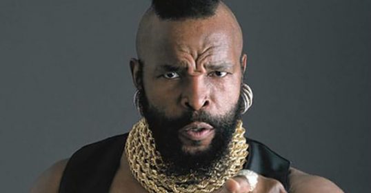 A black man with a beard pointing his finger in a gesture of determination.