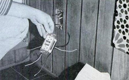 A person holding a box with wires next to an outlet.