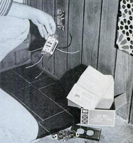A person holding a box with wires next to an outlet.