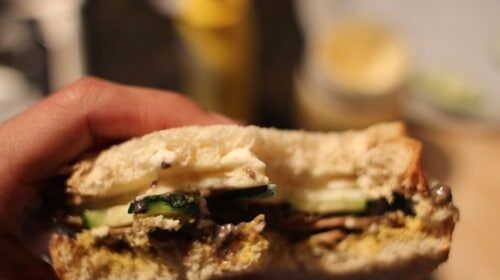 A person holding a Black Bean Veggie sandwich with mushrooms and zucchini.