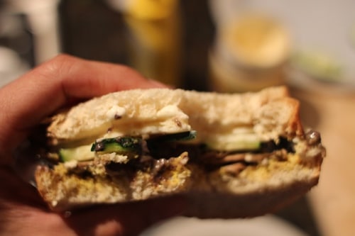 A person holding a Black Bean Veggie sandwich with mushrooms and zucchini.