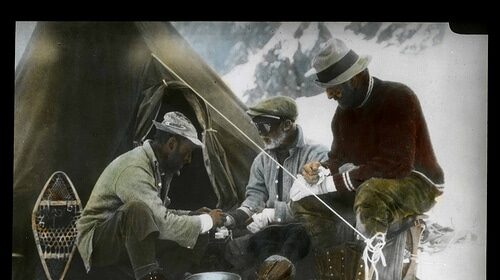 Three men sitting around a tent in the snow, engaged in a profound manvotional discussion.