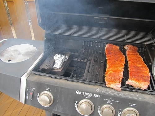 Smoking homemade barbecue pork ribs on grill wood chip box.