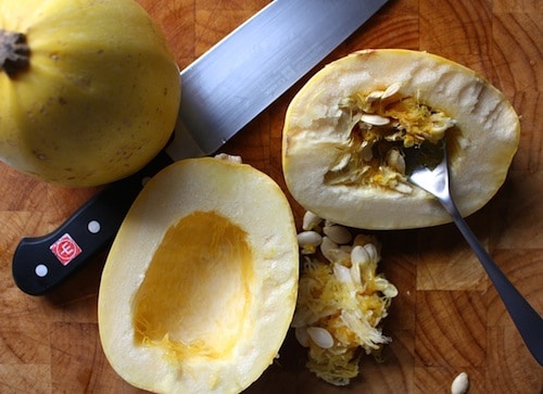 Spaghetti squash scooping seeds with spoon and knife.