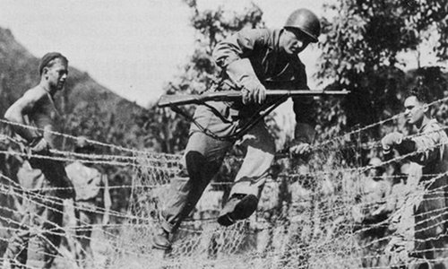 Vintage soldier training jumping over barbed wire fence.