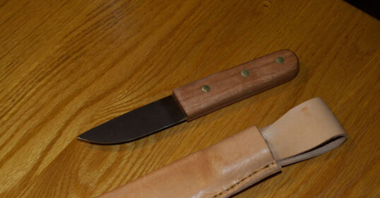 A knife with a leather handle and a wooden sheath on a table.