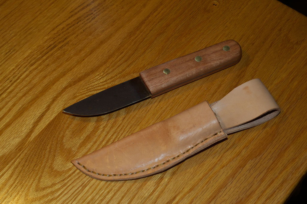 A knife with a leather handle and a wooden sheath on a table.