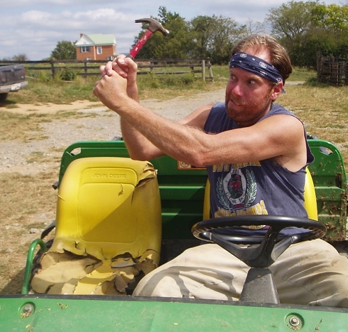 Man sitting in a tractor, holding hammer in both hands.
