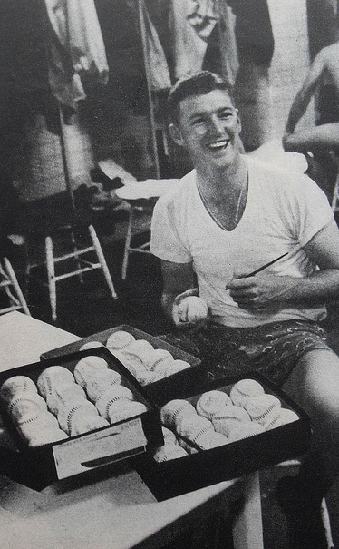 A man wearing undershirts sits at a table surrounded by boxes of donuts.
