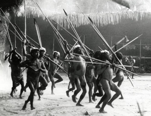 A group of Yanomamö tribe members wielding spears, showcasing the origins and male honor of their community in the sandy landscape.