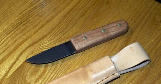 An old knife with a leather sheath on a wooden table.
