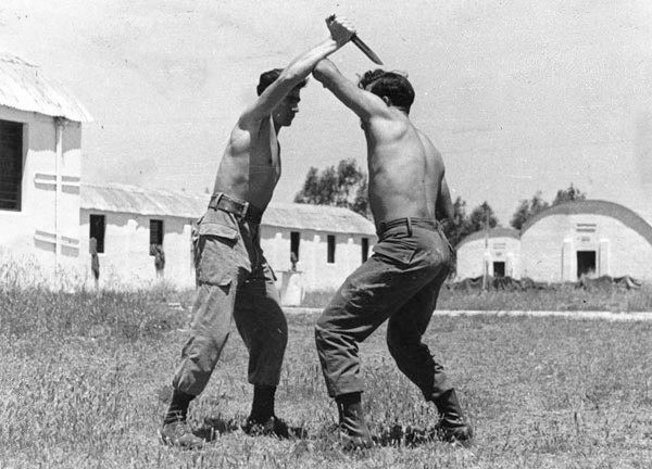 Two men, skilled in a Combative System, engage in a knife fight in a field.
