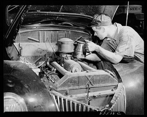 Vintage car auto mechanic working on engine under hood.