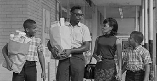 A group of people, with bags in hand, walking down a street.