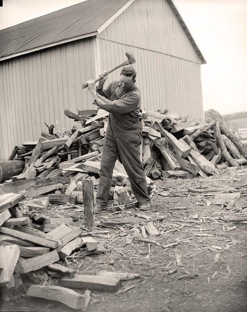 vintage man splitting wood pile of logs around him 