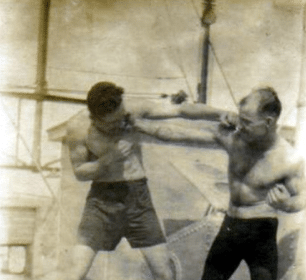 Two men on a boat practicing boxing and taking a punch.