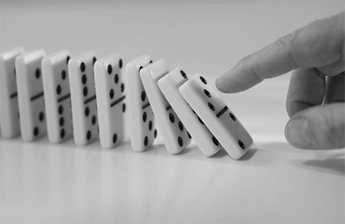 Domino chain being pushed down with finger close up.