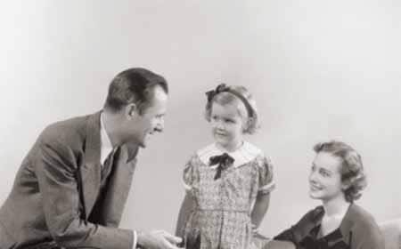 An old black and white photo capturing a moment of positive family culture as a man and woman create a meaningful connection by engaging in conversation with a little girl.
