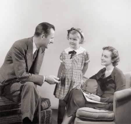 An old black and white photo capturing a moment of positive family culture as a man and woman create a meaningful connection by engaging in conversation with a little girl.