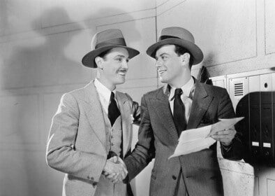 Two men in suits and hats meeting someone next to a mailbox.