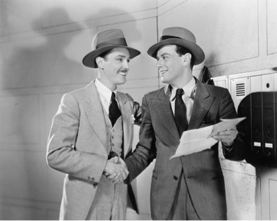Two men in suits and hats meeting someone next to a mailbox.